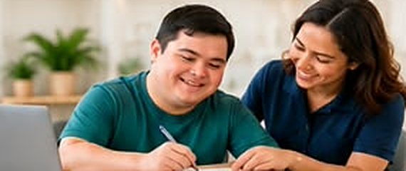 Young man writing at a table with a support worker